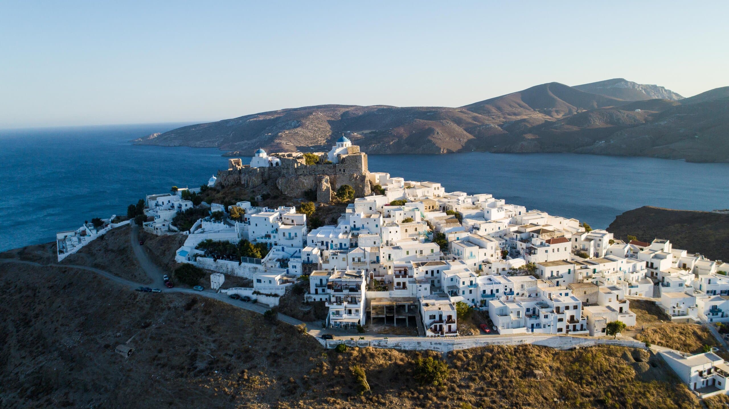 Aerial view of a whitewashed Greek island village overlooking the blue sea.